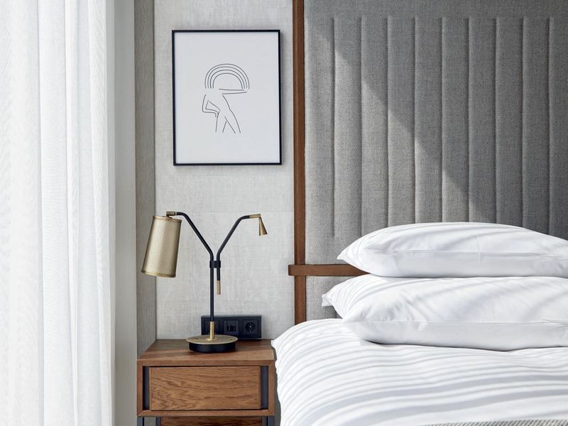 Bedside table with a brass lamp beneath a framed line-art print