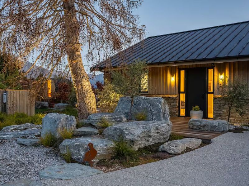 Modern home exterior at dusk, framed by native landscaping and a boulder garden